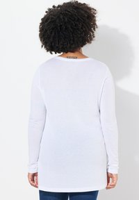 Witte lange mouwen shirt met een ronde halslijn. Zachte, lichte stof. Rechte snit met een gebogen hele, in combinatie met blauwe jeans.