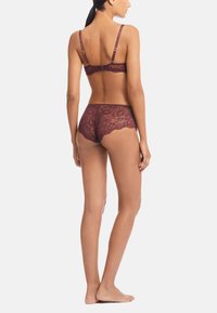 Spets-bh och trosor i djup burgundy, med vågiga kanter och justerbara band, som visar ett fint blommönster.