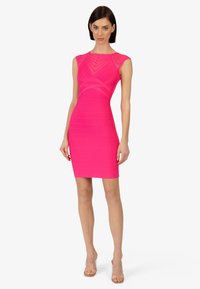 Tætsiddende kjole med kap-sleeves i lys pink med teksturede vandrette striber og udskæringer, parret med gennemsigtige hælede sandaler.