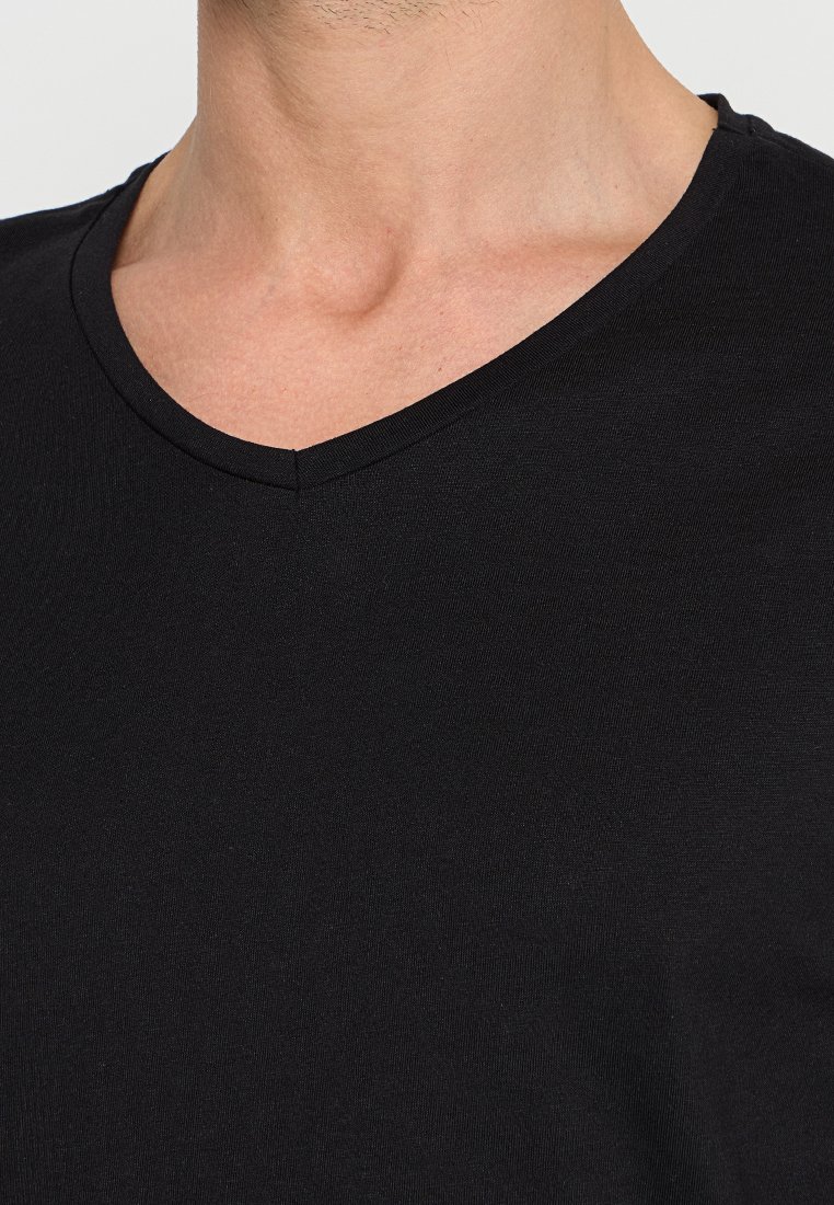 Maglietta nera a V in tessuto morbido, con una trama liscia e linee pulite, caratterizzata da un delicato dettaglio di cucitura lungo il collo.