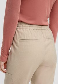 Lichtbeige broek met een zachte textuur, elastische tailleband en subtiele achterzakken, gecombineerd met een getailleerde, geribbelde top in stofroze.