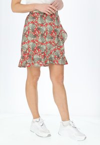Gonna rossa con un motivo paisley bianco e nero. Presenta un orlo svasato e tasche, realizzata in tessuto leggero, indossata con sneakers bianche.