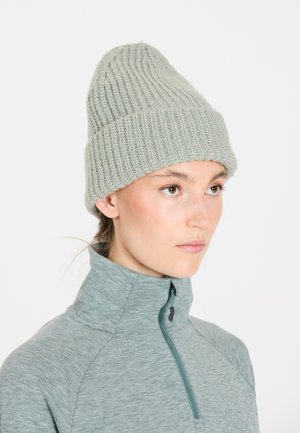 Lysegrønt strikket beanie med ribbet tekstur. Bæres over en grå atletisk top med lynlås og høj krave. Blødt uldlignende materiale.