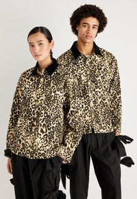 Beige és fekete leopárdmintás kabátok, gombos el�ülső résszel és fekete bársonykalappal, laza fekete nadrágokkal, masnis részletekkel párosítva.