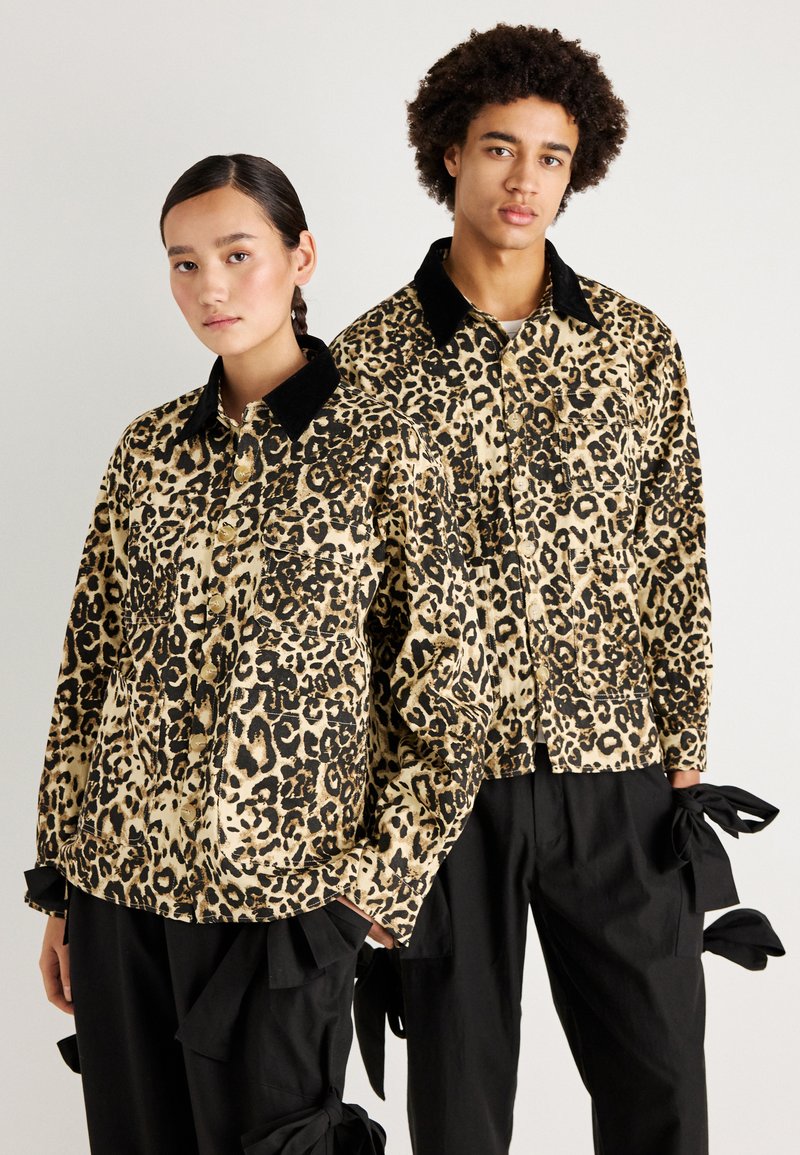 Beige és fekete leopárdmintás kabátok, gombos elülső résszel és fekete bársonykalappal, laza fekete nadrágokkal, masnis részletekkel párosítva.