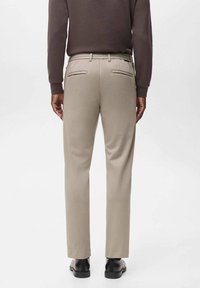 Beige Hosen mit taillierter Passform, ausgestattet mit einem elastischen Bund, zwei Gesäßtaschen und einem glatten, strukturierten Stoff.