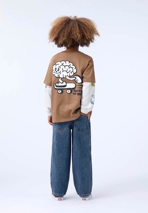 Hnedé oversized tričko s karikatúrou mozgu na skateboarde; skombinované s širokými modrými džínami. Biele rukávy sú zdobené farebnými grafikami.