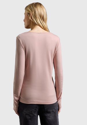 Dlouhý rukáv top v jemné růžové látce s kulatým výstřihem a přiléhavým střihem. Jemná textura a čistý design, kombinované s tmavými džínami.