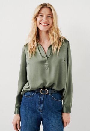 Blouse en satin vert olive à manches longues avec un décolleté en V, associée à un jean en denim bleu et une ceinture noire avec une boucle en or.
