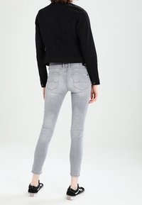 Black denim jacket, fitted design, gray skinny jeans, noticeable stitching on pockets, paired with black sneakers, minimalistic style.