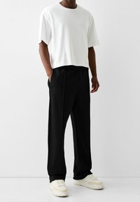 Vit kortärmad T-shirt i kombination med svarta avslappnade byxor, med en mjuk textur och sidofickor, fulländat med krämfärgade sneakers.