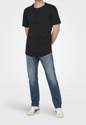 Zwarte T-shirt met korte mouwen en een ronde hals, gecombineerd met lichtblauwe jeans en witte sneakers met zwarte accenten.