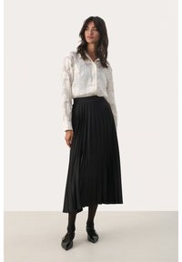 Valge pika varrukaga pluus lille tikandiga, koos musta volditud midi-seelikuga. Mustad pahkluu pikkuses sukkpüksid ja terava ninaga kingad lisavad riietusele elegantsi.
