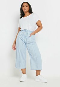 Culottes de denim azul claro con una cintura elástica y cordón. Cuenta con bolsillos y un corte relajado. Combinados con una camiseta blanca y zapatillas.