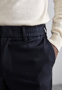 Marineblauwe broek met een elastische tailleband, een gladde textuur en zijzakken. Draagt samen met een lichtbeige trui, wat een casual stijl benadrukt.