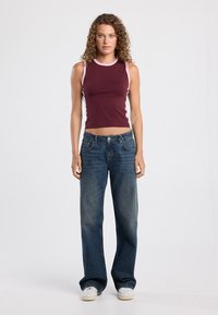 Burgundy sleeveless top with pink trim, paired with wide-leg blue jeans. The outfit features casual footwear and a relaxed fit overall.