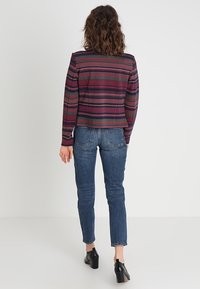 Strickjacke mit einem mehrfarbigen Muster aus Streifen und Zickzacks, langen Ärmeln und einem verkürzten Design, kombiniert mit enganliegenden Jeans.