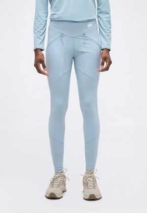 Person wearing light blue fitted leggings with drawstrings and beige athletic shoes, standing against a plain background.