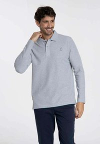 Polo gris à manches longues en tissu doux, avec un col et trois boutons, comportant un petit logo brodé sur la poitrine.