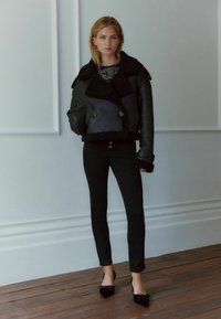 Melna aitene ar dubultu pogu dizainu, liela apkakle, melni skinny džinsi un melnas, norādītas lakotas kurpes ar loku akcentiem.