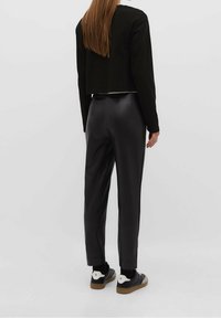 Zwarte cropped jack gecombineerd met glanzende zwarte faux leren broeken. Sneakers met een zwarte body en witte accenten maken de look compleet.