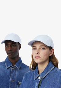 Due persone indossano cappellini azzurri chiari e giacche di denim. I cappellini sono strutturati e presentano una visiera leggermente curva.