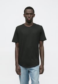 Černé bavlněné tričko s kulatým výstřihem, krátkými rukávy a zaobleným lemem. V kombinaci se světle modrými džínami. Hladká textura, bez vzorů.