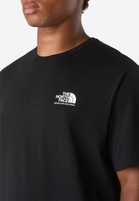 Närbild av en person som bär en svart T-shirt med "The North Face"-logotypen och sloganen "Never Stop Exploring" på vänster bröst.