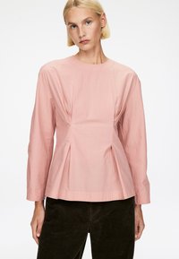 Helles rosa Blusenshirt mit langen Ärmeln, rundem Ausschnitt und plissierten Details an der Taille. Der Stoff sieht glatt aus und hat eine minimale Textur.