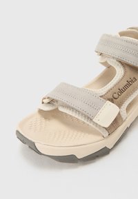 Light-colored sandal featuring adjustable gray straps, textured insole, and a sturdy sole. Brand name "Columbia" visible on the side.
