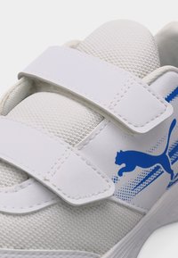 Λευκό αθλητικό παπούτσι με δύο λουριά Velcro και μπλε λογότυπο Puma στο πλάι, που διαθέτει υφασμάτινο πλέγμα και ομαλό συνθετικό υλικό.