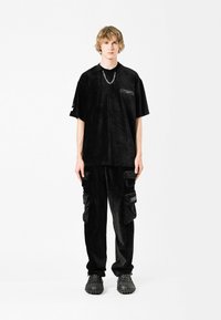 Camiseta oversized de terciopelo negro con un bolsillo en el pecho y diseño texturizado, combinada con pantalones cargo negros a juego con bolsillos laterales.