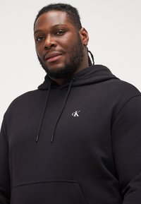 Black hoodie made from a soft fabric, featuring a front pocket, drawstrings, and a small white "ck" logo on the chest.