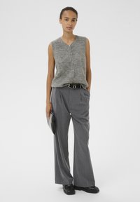 Harmaa neulottu ilman hihoja oleva toppi, jossa on napit, yhdistetty korkeavyötäröisiin, leveälahkeisiin raitapantseihin. Malli pitää mustaa clutch-laukkua.