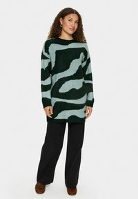 Maglione a maniche lunghe con motivo verde e azzurro chiaro, vestibilità comoda, texture morbida e polsini a coste, abbinato a pantaloni neri a gamba larga.