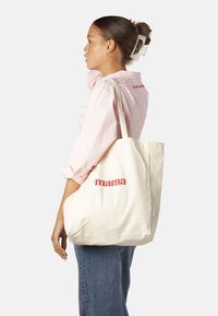 Borsa a tracolla in tela di colore crema con il testo "mama" rosso, dotata di manici robusti e di un design spazioso e strutturato.