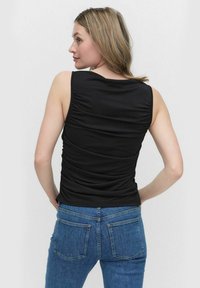 Svart ärmlös topp med rynkad textur på baksidan, matchad med blå denimjeans som har två bakfickor och en lätt stretch.