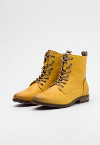 Żółte skórzane botki za kostkę z zaokrąglonymi palcami, sznurowane z przodu, z dekoracyjnym akcentem w leoparda na kołnierzu. Płaska pięta i gładka tekstura.