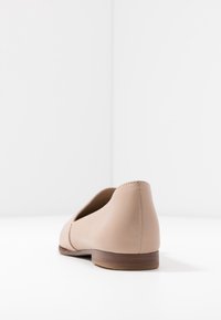 Ballerines en cuir beige avec une texture lisse, bout arrondi et petit talon en bois, présentant des détails de couture minimaux le long de l'arrière.