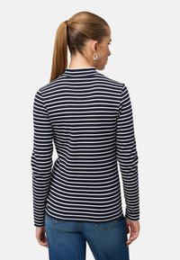 Tričko s dlhým rukávom a vysokým golierom, s námorníckymi a bielymi horizontálnymi pruhmi, vyrobené z mäkkej látky, v kombinácii s modrými džínsami.
