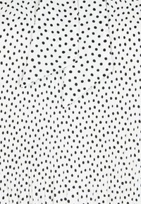 Weißer Stoff mit schwarzen Punkten, ausgestattet mit einem plissierten Design und einer Schleifendetail am Ausschnitt. Glatte Textur insgesamt.