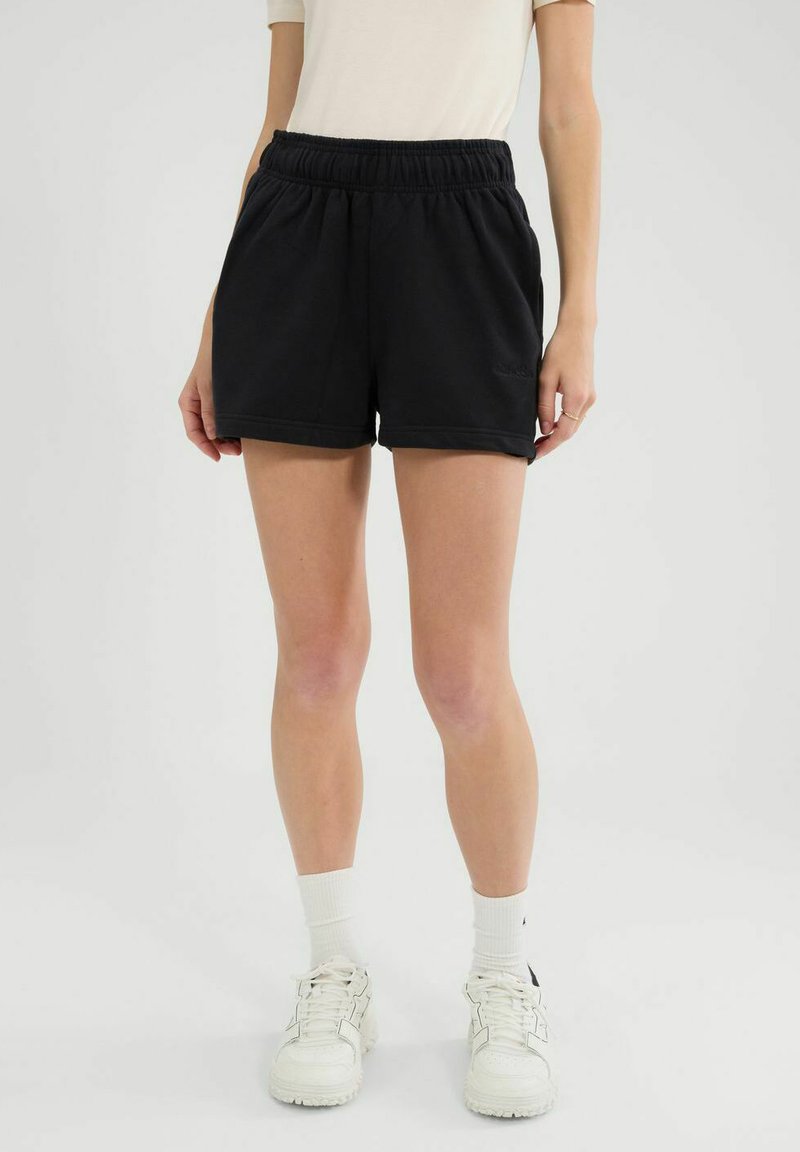 Shorts de algodón negros con cintura elástica, bolsillos laterales y un ajuste relajado, combinados con zapatillas blancas y calcetines de longitud media.