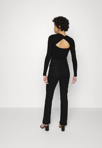 Top preto de mangas longas com um recorte nas costas, combinado com jeans pretos de perna reta e sandálias pretas de salto bloco. Textura suave.