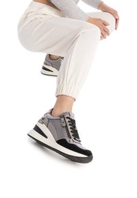 Zapatillas gris y negras con un diseño elegante, que cuentan con una parte superior texturizada, cierre de cordones en la parte delantera, detalle de cremallera y una suela blanca contrastante.