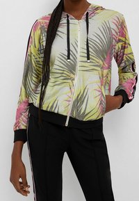 Hooded zip-up jack met een kleurrijke palmbladenprint, metallic glans, zwarte accenten en contrasterende zijdelingse strepen. Gemaakt van lichtgewicht materiaal.