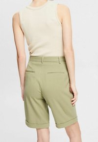 Débardeur côtelé beige associé à un short vert olive à mi-cuisses, avec des manches retroussées et deux poches arrière. Texture de tissu lisse.
