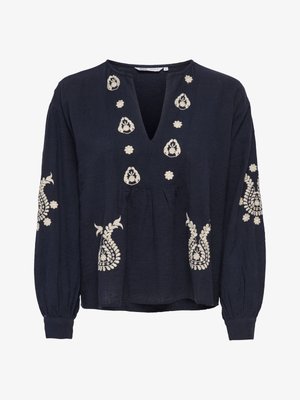 Blusa azul marino de manga larga con bordado floral blanco en el pecho, las mangas y la parte inferior delantera, con cuello en V.