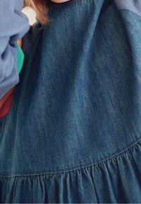 Abito in denim con vita arricciata e colori contrastanti. Presenta una texture in denim blu, vestibilità rilassata e scollatura rotonda.