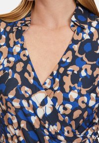 Wrapklänning i mörk marin med ett leopardmönster som har blå, beige och vita accenter; har en V-ringning och kort krage.
