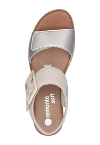 Sandales Remonte en toile beige avec une lanière en métal argenté. Équipées d'une boucle robuste et d'une semelle intérieure texturée marron pour plus de confort.